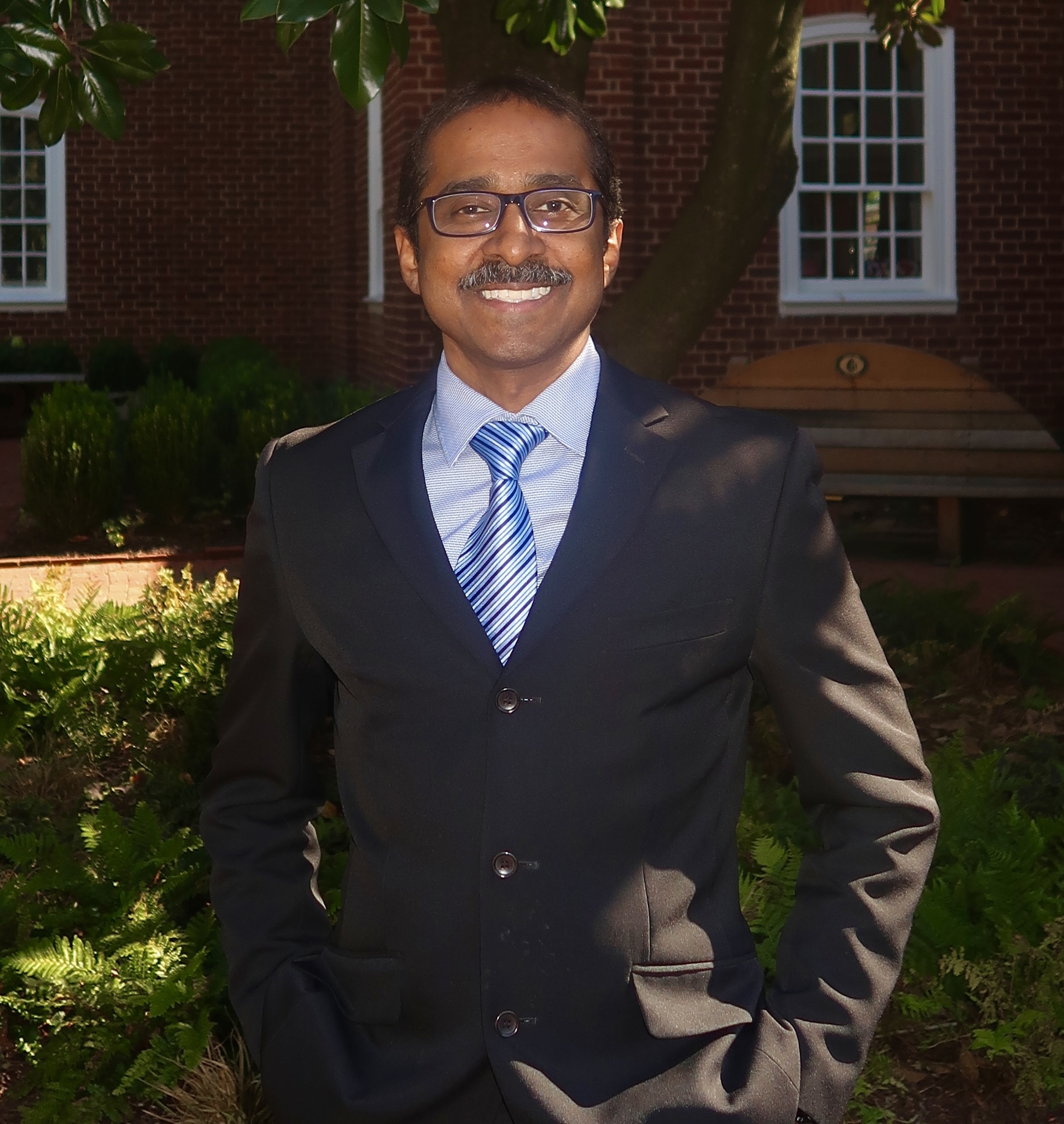 Jay Arasan, Associate Director smiling in front of world map